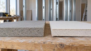 Muestra de placa homogénea con fibras junto a una placa de yeso con revestimiento de papel en un taller de construcción