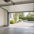 Interior de un garaje residencial con una puerta seccional parcialmente elevada, guías bajo el techo y acceso despejado.